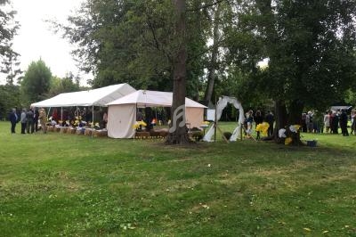 Tentes blanches installées dans un parc verdoyant, entourées de personnes et de décorations jaunes et blanches.