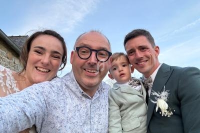 Un groupe de quatre personnes souriantes, dont un enfant, posant en extérieur sous un ciel bleu.