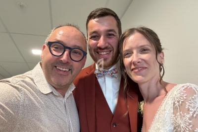 Trois personnes souriantes posant pour une photo, dont un couple en tenue de mariage dans un intérieur lumineux.