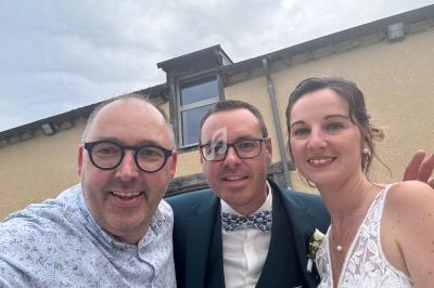 Un groupe de trois personnes souriantes posant devant un bâtiment beige avec une fenêtre en arrière-plan.