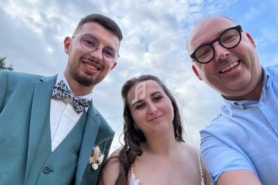 Trois personnes souriantes posent pour une photo en extérieur sous un ciel partiellement nuageux.