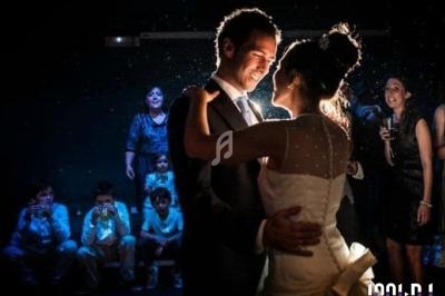 Un couple danse sous un éclairage tamisé, entouré d'invités souriants lors d'une célébration.