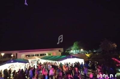 Foule rassemblée de nuit devant des stands éclairés sous des tentes, dans un espace extérieur.