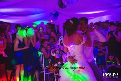 Un couple de mariés danse au centre d'une salle éclairée de lumières colorées, entouré d'invités attentifs.
