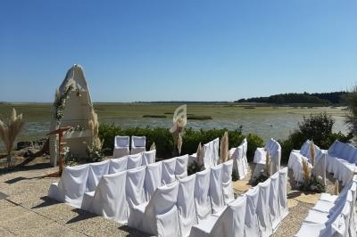 Chaises blanches alignées pour une cérémonie en extérieur, avec vue sur un paysage naturel de marais et ciel dégagé.