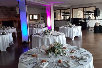 Salle de réception décorée avec des tables rondes dressées, nappes blanches et centres de table floraux.