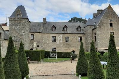 Façade en pierre d'un manoir historique avec tours, jardin aménagé et allée bordée de conifères taillés.