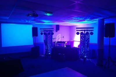 Salle équipée de matériel de sonorisation et éclairage coloré, avec une scène et un écran de projection.