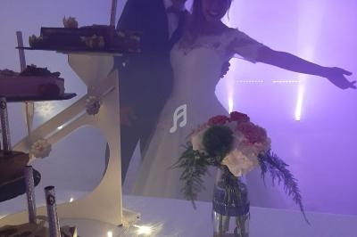 Un couple en tenue de mariage pose joyeusement devant une table décorée avec des gâteaux et un bouquet de fleurs.