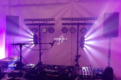 Équipement de DJ avec platines, micros, enceintes et éclairages colorés dans une salle éclairée en violet.
