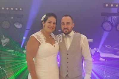 Un couple en tenue de mariage pose devant des lumières colorées dans une ambiance festive.