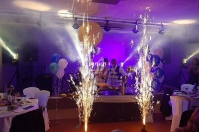 Fontaine de feux d'artifice illuminant une salle de réception décorée avec des ballons et des tables dressées.