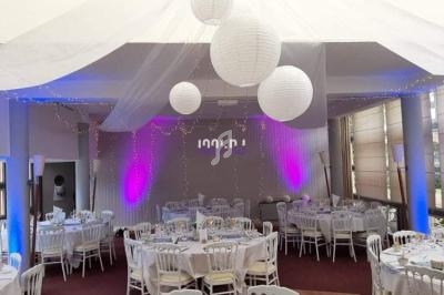 Salle de réception décorée avec des tables rondes, des chaises blanches, des lanternes suspendues et des éclairages colorés.