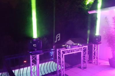 Jeux de lumières verts et violets éclairant une terrasse avec une table de mixage près d'une piscine la nuit.