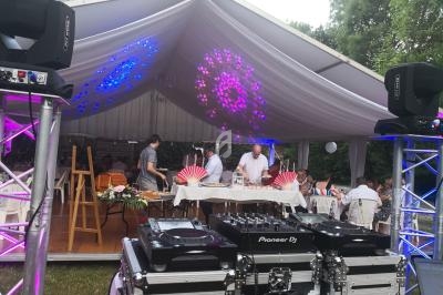 Tente blanche décorée pour un événement, avec buffet, invités et matériel de DJ au premier plan.