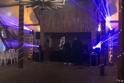 Deux personnes ajustent un équipement de DJ sous des jeux de lumière dans une salle avec murs en bois et briques.