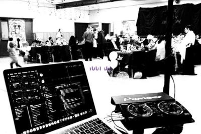 Vue d'une salle de réception avec des invités attablés, prise depuis une table de DJ équipée d'un ordinateur portable.