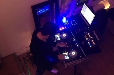 Vue plongeante sur un DJ mixant sur une table équipée de platines et d'un ordinateur dans une pièce éclairée.