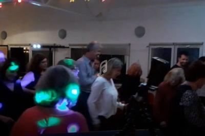 Des personnes dansent dans une salle éclairée par des lumières colorées, avec des fenêtres en arrière-plan.