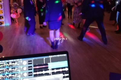 Des personnes dansent dans une salle éclairée par des lumières colorées, avec une table de mixage en premier plan.