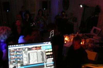 Vue d'une soirée animée avec des invités dans une pièce sombre, un écran de DJ au premier plan.