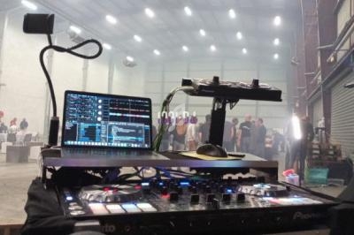 Table de mixage avec équipements DJ, écrans et casque, dans une grande salle éclairée avec des personnes en arrière-plan.