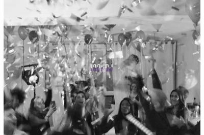 Des personnes célèbrent dans une pièce décorée avec des confettis et des ballons en suspension.