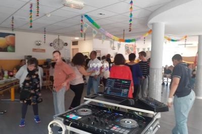 Des personnes dansent dans une salle décorée avec des guirlandes colorées, un équipement de DJ au premier plan.