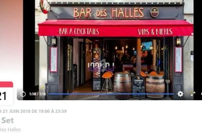 Façade du bar ’Bar des Halles’ avec terrasse, tonneaux en bois et enseigne rouge, vue depuis la rue.