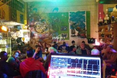 Vue d'un café animé avec des personnes discutant, un mur décoré de fresques et un écran d'ordinateur au premier plan.