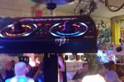 Console de DJ éclairée dans un bar animé avec des décorations suspendues, dont un vélo au plafond.