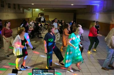 Des personnes dansent sur une piste éclairée par des lumières colorées dans une salle de réception.