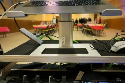 Ordinateur portable affichant un logiciel de mixage audio, posé sur un support au-dessus d'une table de mixage DJ.