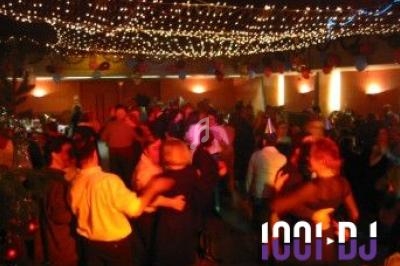 Des personnes dansent sous des guirlandes lumineuses dans une salle décorée pour une fête.