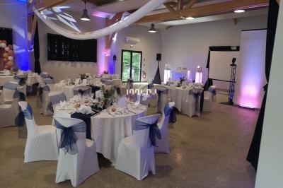 Salle de réception décorée avec des tables rondes dressées, chaises blanches ornées de nœuds bleus et éclairage d'ambiance.