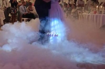 Un couple danse au milieu d'une piste enveloppée de fumée, sous le regard des invités assis autour.