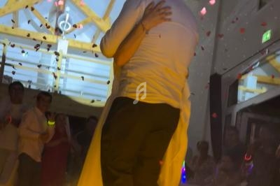 Un couple s'enlace sur une piste de danse entourée de fumée et de pétales, sous des lumières tamisées.