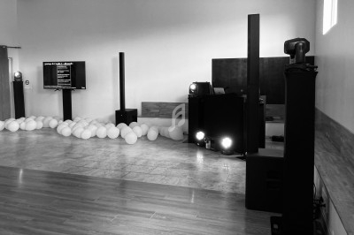 Salle de réception avec équipement audio, éclairage et ballons blancs dispersés au sol.