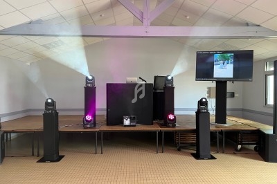 Quatre projecteurs lumineux entourent une table avec un ordinateur et un écran dans une salle équipée pour un événement.