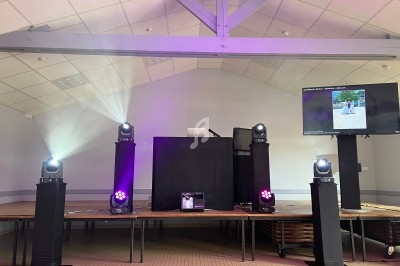 Scène équipée de projecteurs lumineux, d'un écran et d'un pupitre dans une salle au plafond voûté.