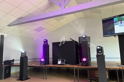 Scène équipée de projecteurs lumineux, d'une table de mixage et d'un écran dans une salle au plafond en poutres apparentes.