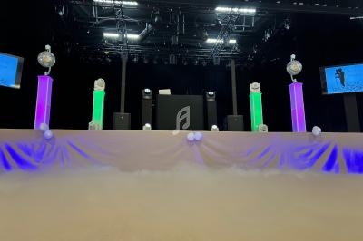 Scène décorée avec des colonnes lumineuses colorées, des boules disco et un fond de fumée sous un éclairage de spectacle.