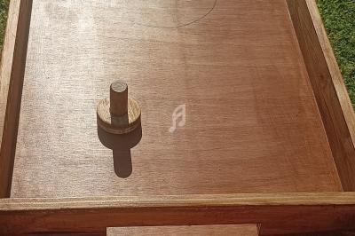 Table de jeu en bois avec deux palets et un plateau rectangulaire, placée sur une pelouse en extérieur.