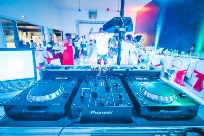 Vue d'une table de mixage Pioneer dans une salle de réception avec des invités dansant en arrière-plan.