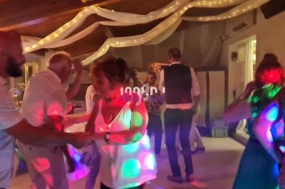 Des personnes dansent dans une salle décorée avec des guirlandes lumineuses, éclairées par des lumières colorées.