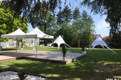 Tentes blanches installées dans un jardin verdoyant avec une terrasse en bois et des arbres en arrière-plan.