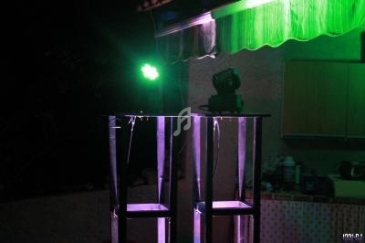 Deux projecteurs lumineux sur des structures métalliques, éclairant une terrasse extérieure la nuit.