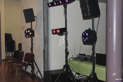 Équipement d'éclairage sur trépieds dans une salle avec des chaises empilées et une table équipée d'appareils électroniques.