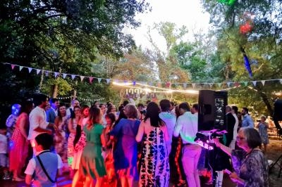 Groupe de personnes dansant en extérieur sous des guirlandes lumineuses, entouré d'arbres et de décorations festives.