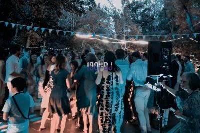 Groupe de personnes dansant en extérieur lors d'une fête, entouré de guirlandes lumineuses et d'arbres.